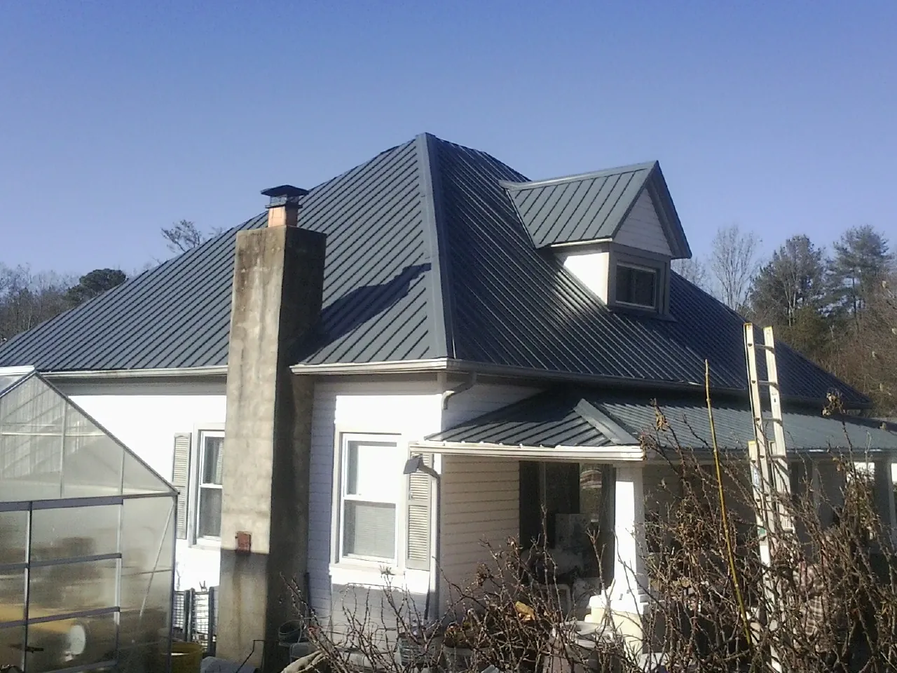 Dark blue standing seam metal roof on a white farmhouse with dormer — Slate & Tile Roof Repair by Roofing Brothers in Delia