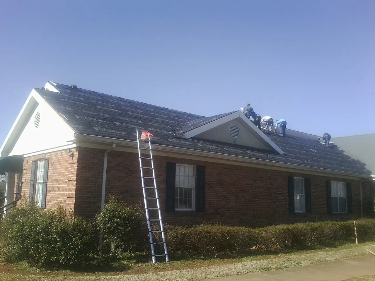 Crew tearing shingles off a brick ranch roof with a ladder set — Emergency Roof Repair work by our crew in Delia