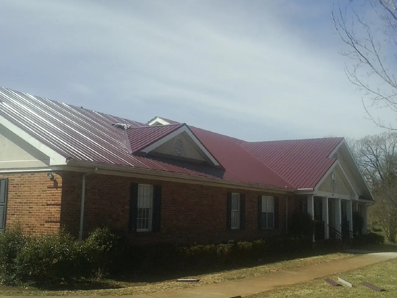 Red metal roof with gabled entries on a long brick building, from a Hail Damage Roof Repair job in Delia