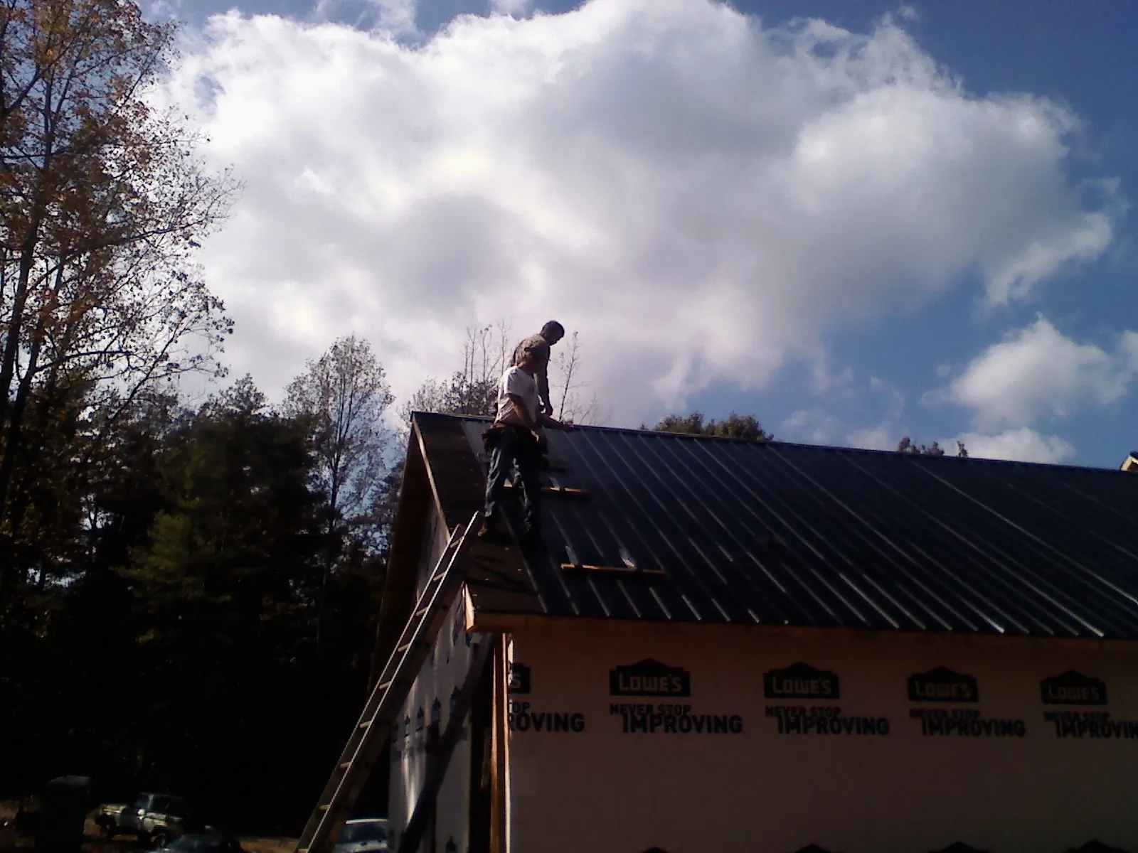 Roofer fastening dark metal panels high against a cloudy sky, from a Roof Inspection job in Delia