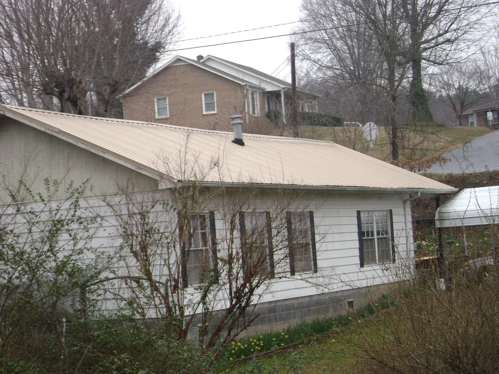 Tan metal roof on a white sided house set into a hillside — Commercial Roofing by Roofing Brothers in Delia